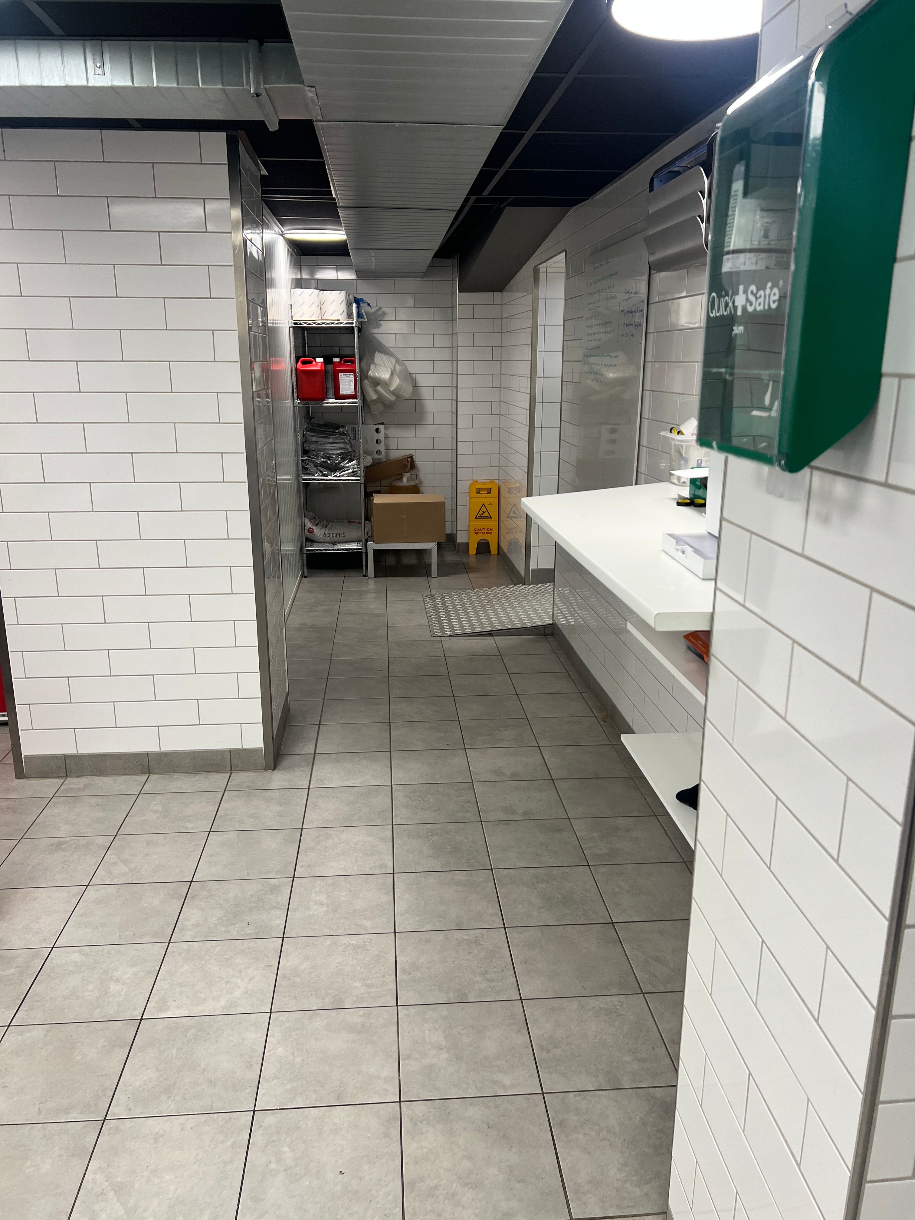 En tom lagerrum med hvide mursten og gulv. Til højre er en hvid bordplade og en køkkenudstyret. Der er en Quick Safe og en skilt.