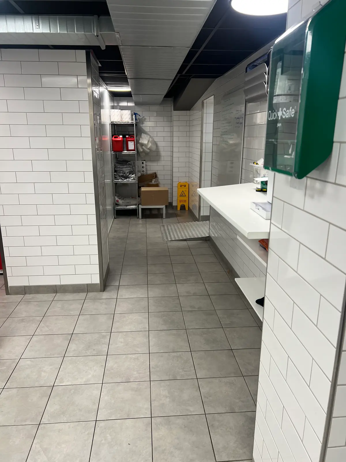En tom lagerrum med hvide mursten og gulv. Til højre er en hvid bordplade og en køkkenudstyret. Der er en Quick Safe og en skilt.