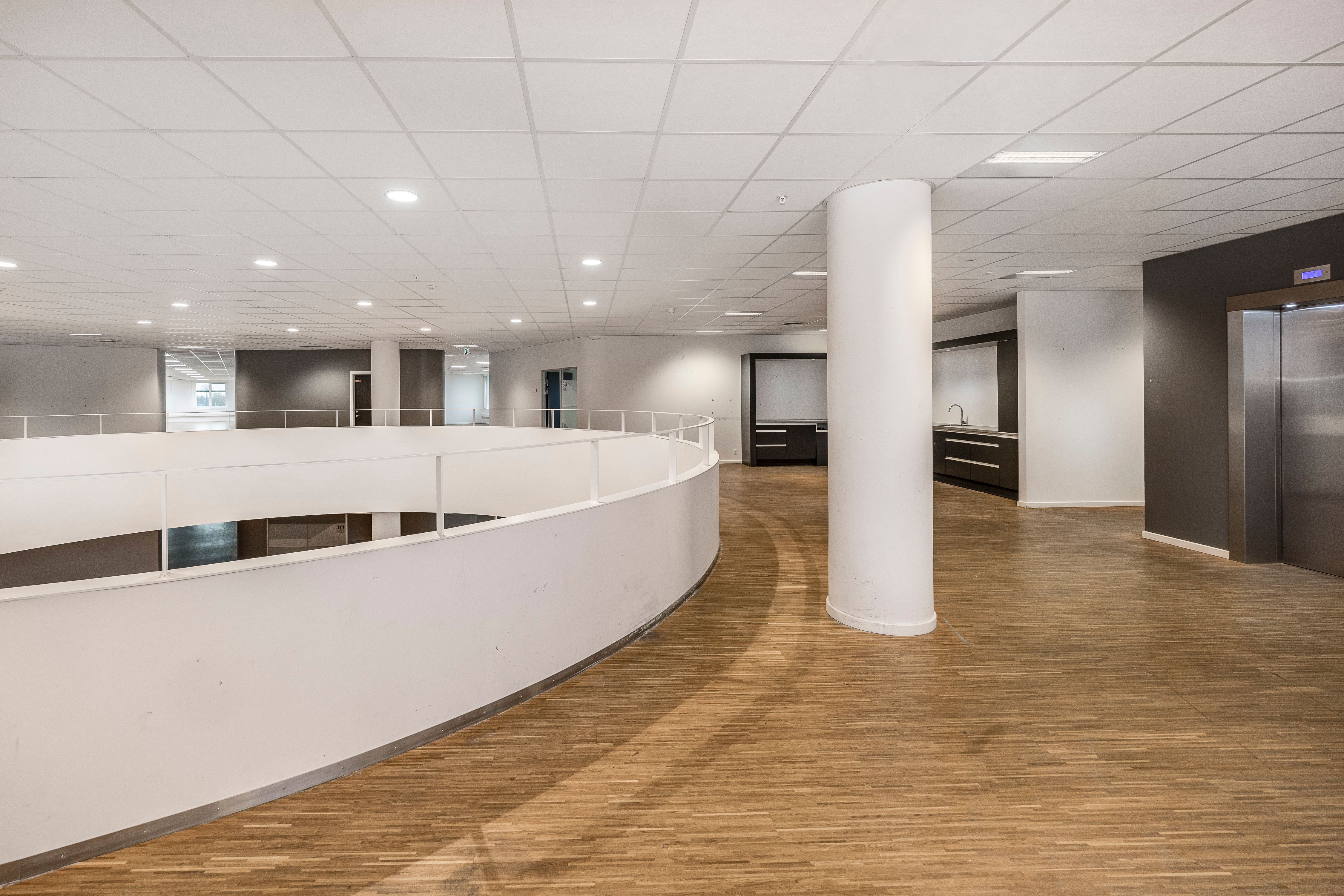 Store, moderne kontorbygning med blanke gulve, lyse lofter og mødecenter i hjørnet. Rundt gulv og loftsventilation, lysepunkter og elevator.