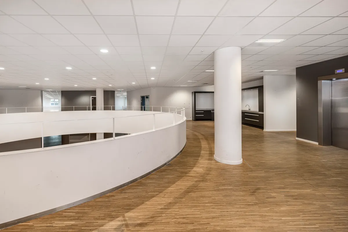 Store, moderne kontorbygning med blanke gulve, lyse lofter og mødecenter i hjørnet. Rundt gulv og loftsventilation, lysepunkter og elevator.