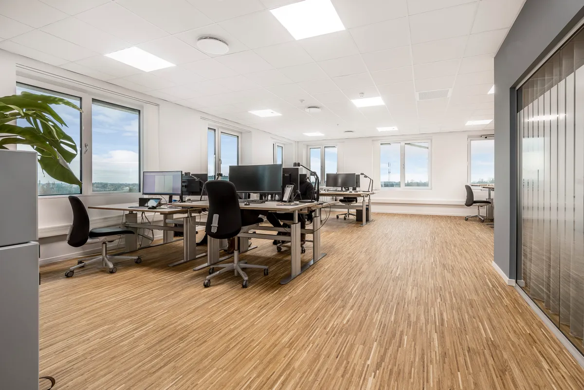 Gladsaxe Company House med trægulve, vinduer, skriveborde, computere, stolpe og plante i hjørnet og fuldt udstyret kontor med lysekroner og glasdøre