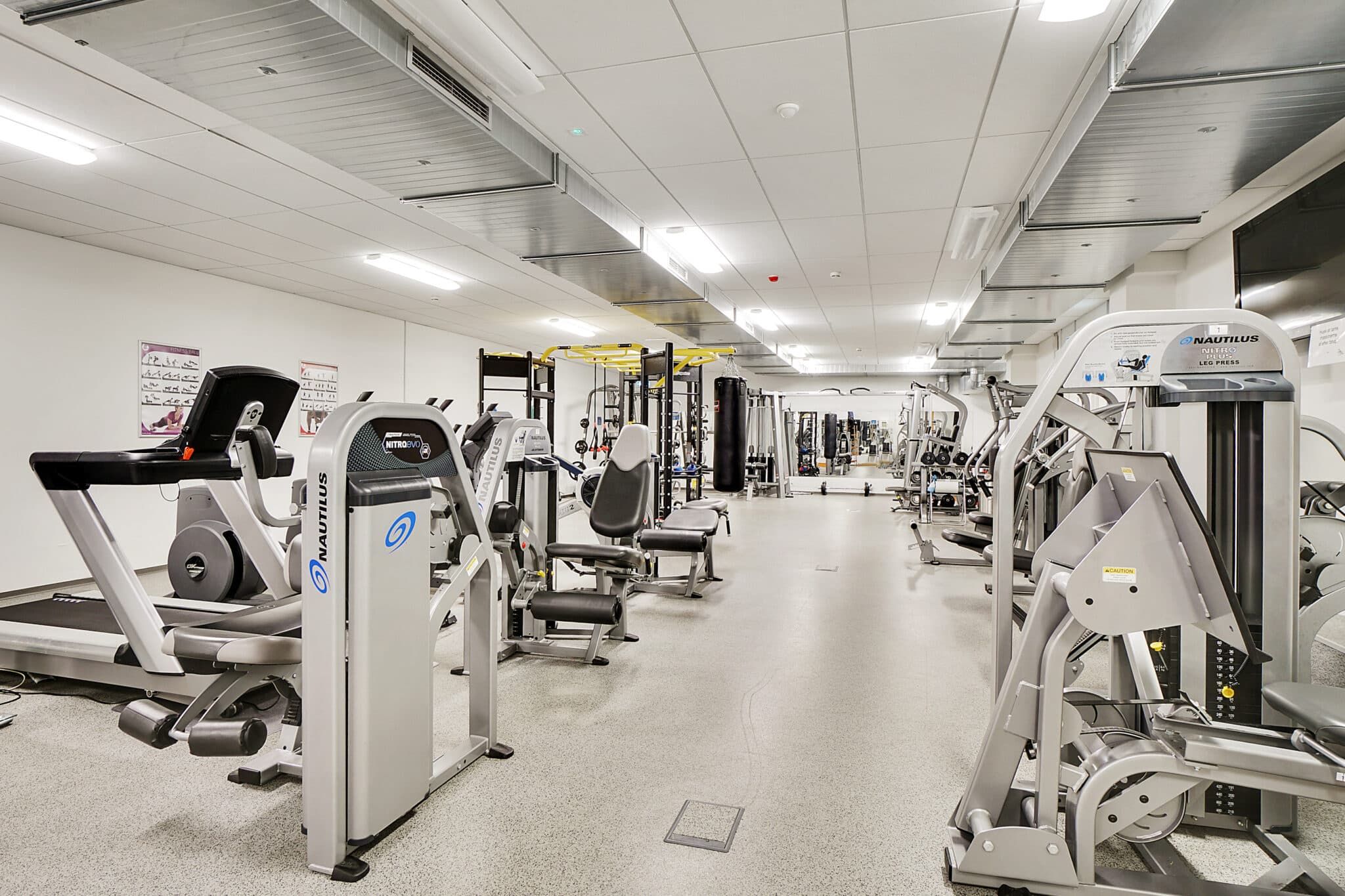 Moderne fitnesscenter med træningsmaskiner og løbebånd, hvor ventilerede lofter og lyse vægge skaber en komfortabel atmosfære for træning.