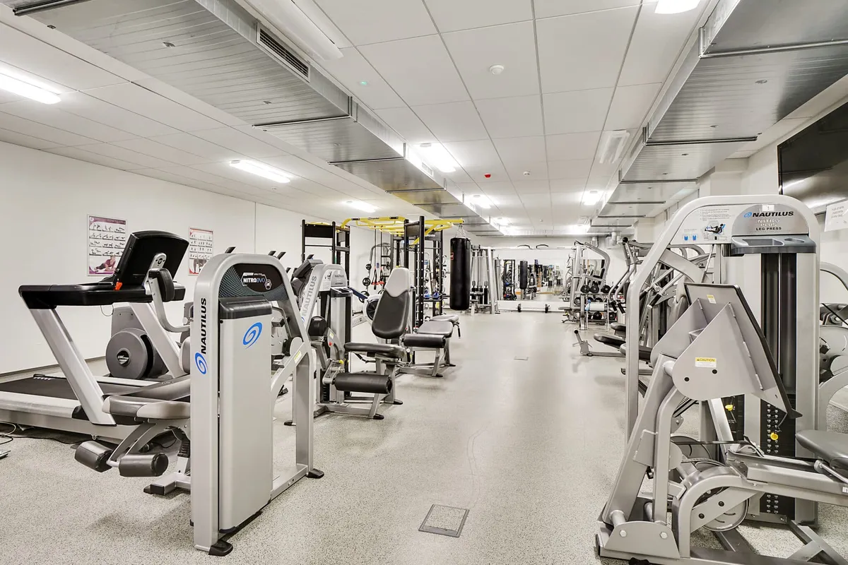 Moderne fitnesscenter med træningsmaskiner og løbebånd, hvor ventilerede lofter og lyse vægge skaber en komfortabel atmosfære for træning.