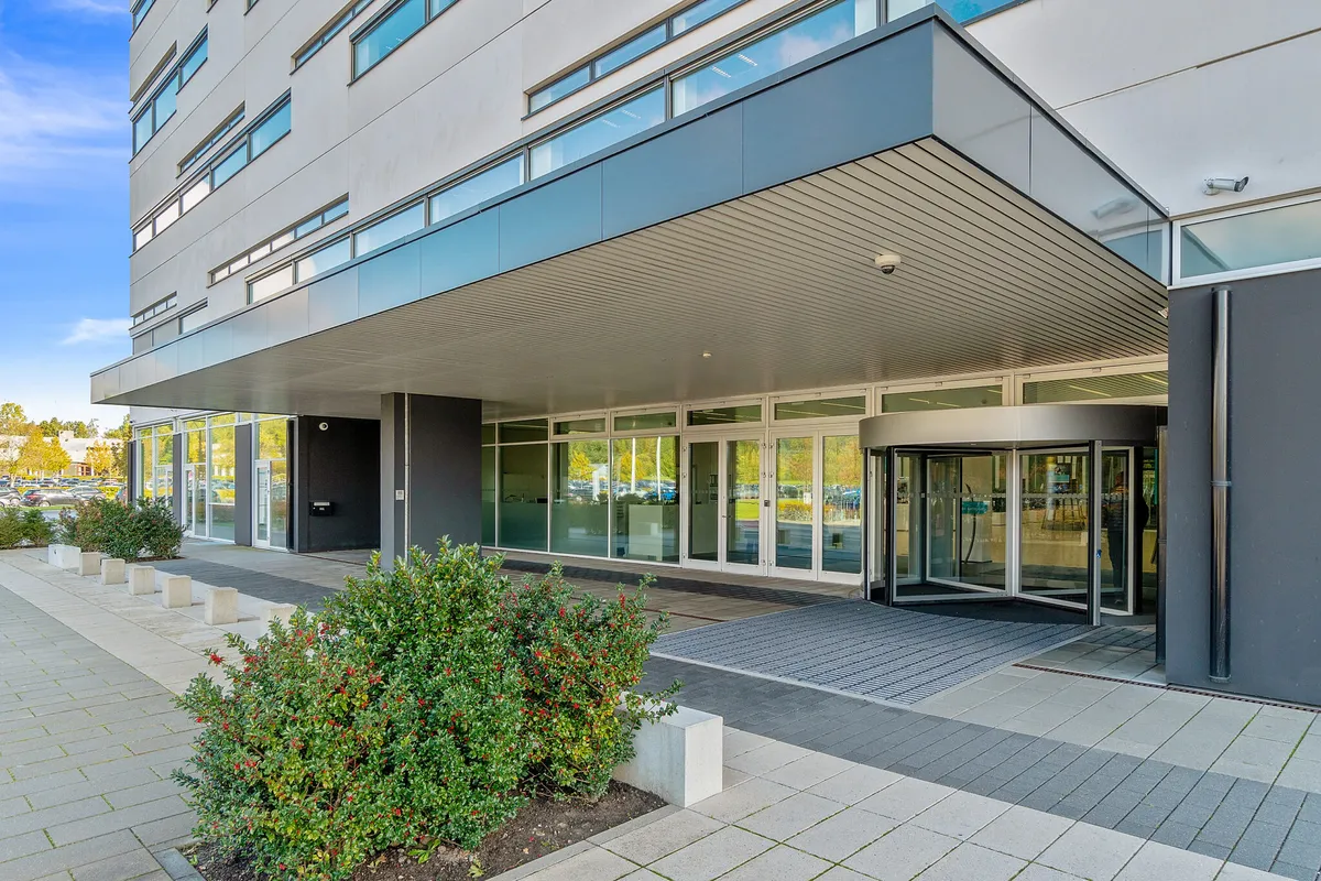 Moderne og elegant kontorlejemål med glasdøre, automatiske drejedøre og eksklusive fællesfaciliteter. Man kan se et stort antal biler parkeret på baggrunden