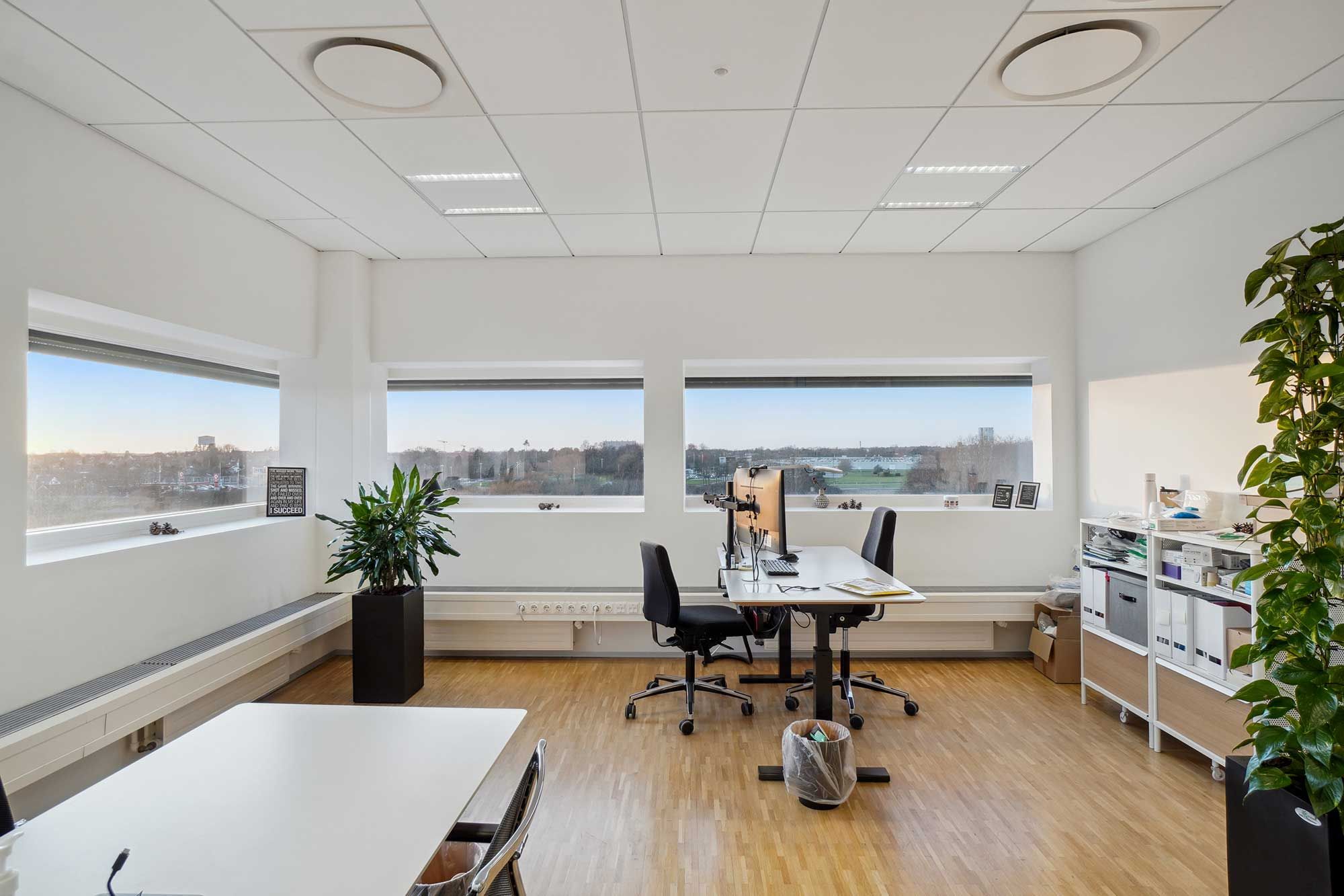 Kontorrum med højt til loftet, hvide vægge, store vinduer, gulve med træpaneler og møbler i sort og hvidt