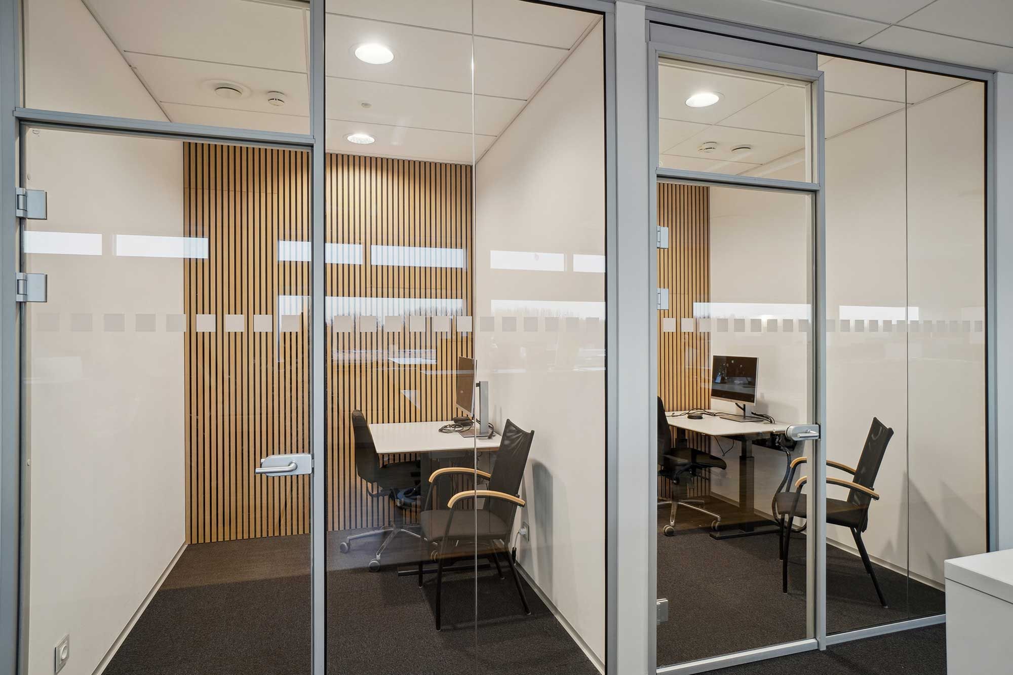 Moderne kontorrum med højt gulv og hvide vægge, hvor to bord med computere og stol er placeret på hver side af rummet