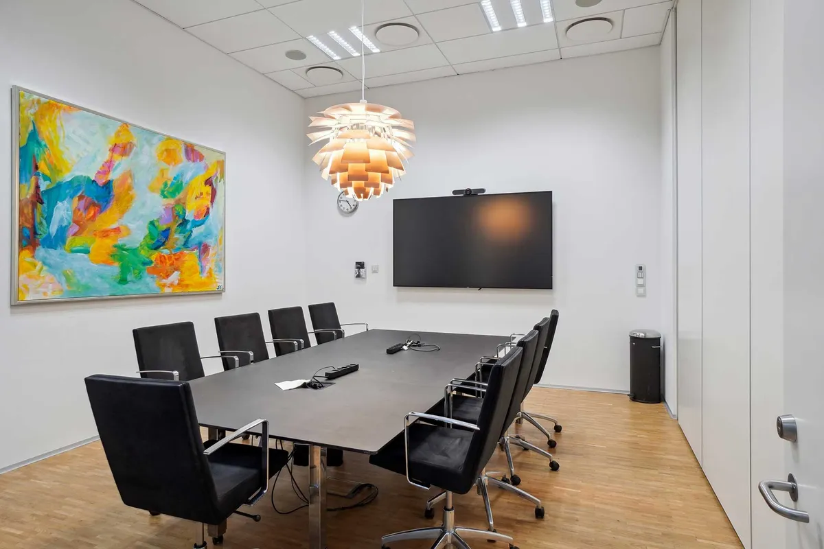 Moderne kontor med højloft, møbelsæt, skrivebord, projektor, kunstværk, stol, åbne døre og en slank søjle i rummet