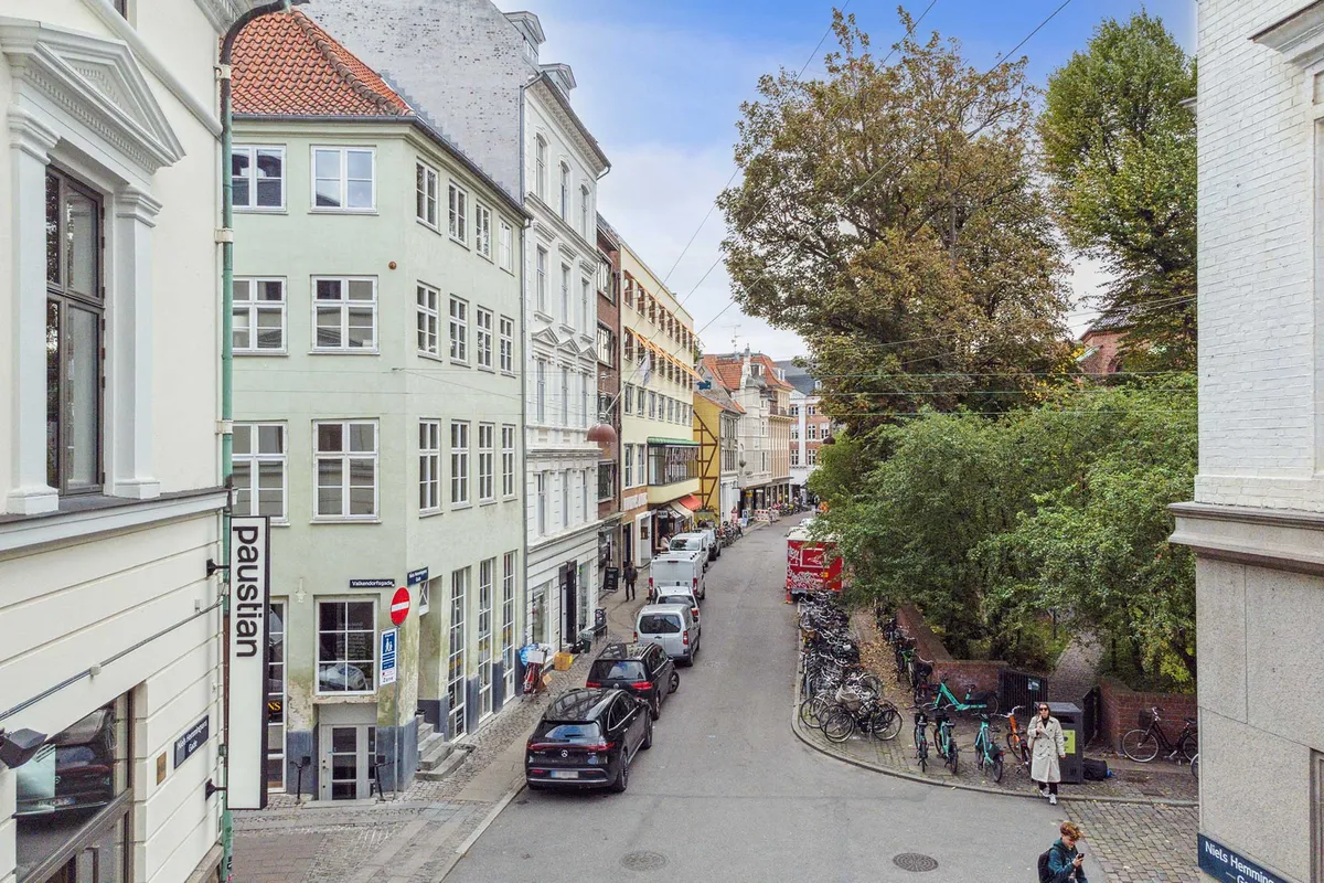 Foto af Valkendorfsgade med to biler parkeret, flere cykler og en person i trenchcoat går på fortovet
