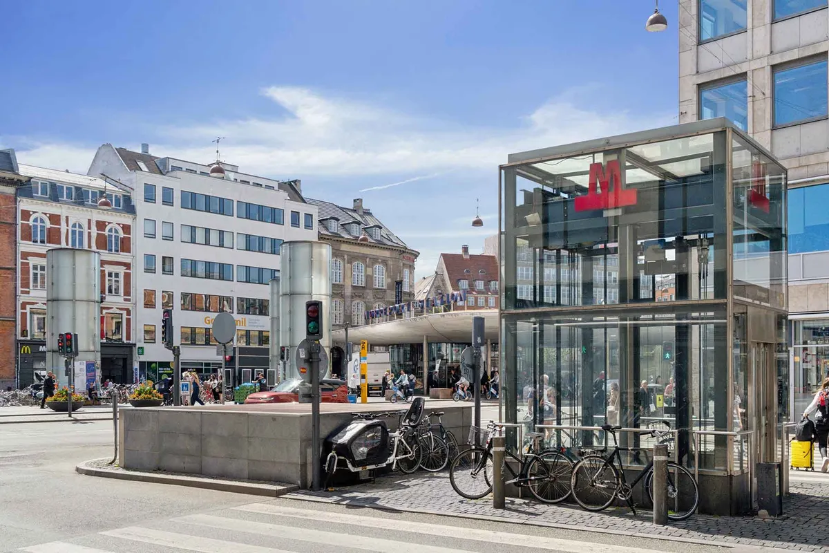 Kontor bygning med busstoppested og cykelparkering, flere gående og cyklende folk og en McDonalds restaurant i baggrunden