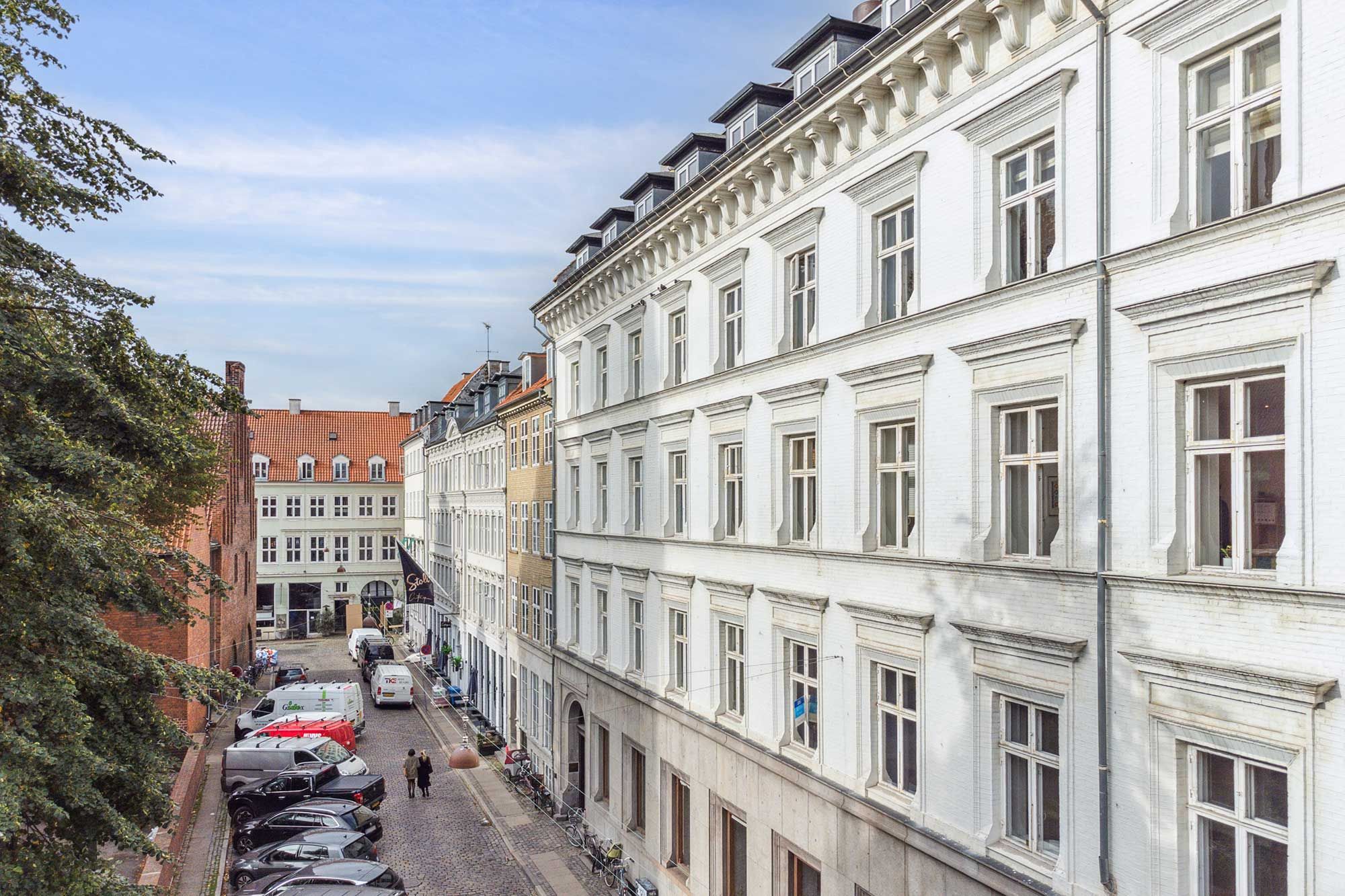 Kontor i charmerende, klassisk bygning med udsigt over København, parkerede biler og enkeltpersoner, høje huse, vinduerne med lysegardiner og hvide vægge