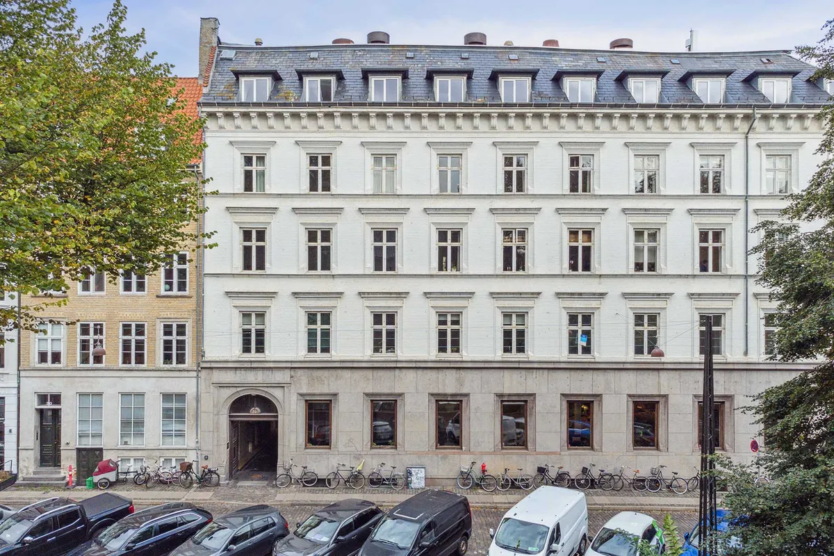 Kontorlejemål med udsigt til gaden og parkeringsplads foran bygningen. Klassisk, hvid, borgerlig bygning med udsigt til grønne træer og parkerede biler