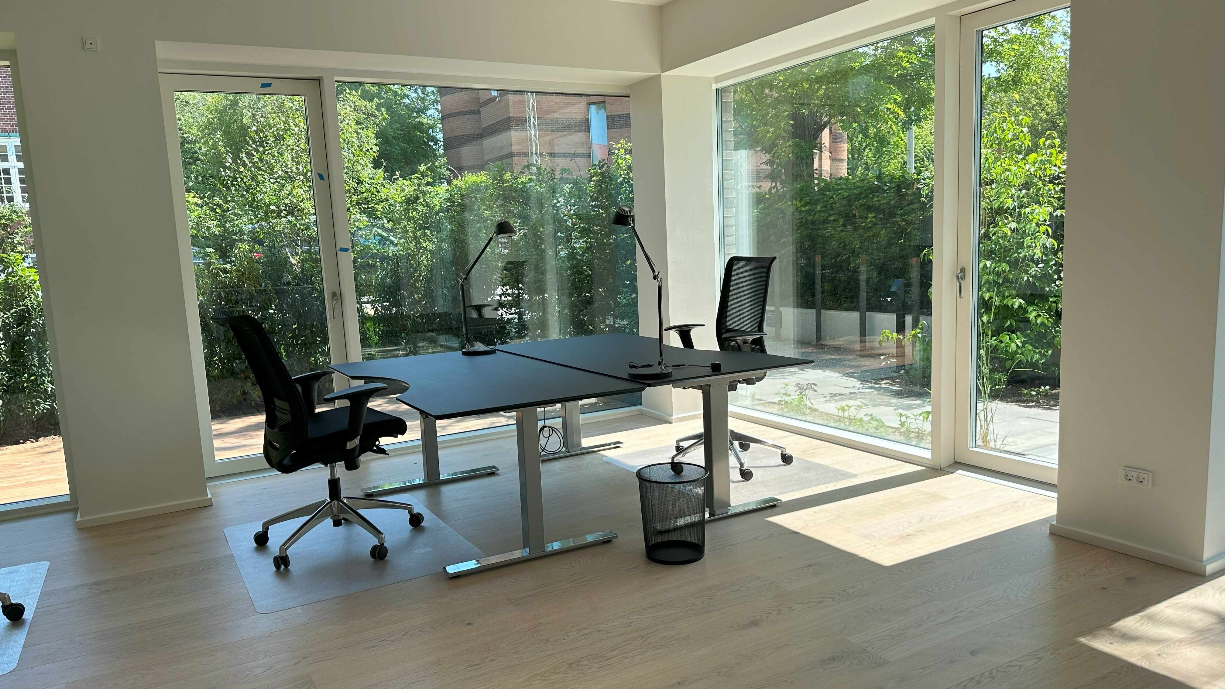 Kontorrum med to skriveborde og to stolpe til at sidde på. Et skrivebord med to skraldespande og et papirkurv på gulvet. To stolpe med hjul og en lampe.