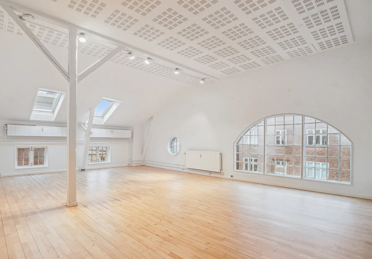 Rummelige kontorlokaler med højloft, hårdt trægulv, lyse loftsvinduer og store glasvinduer mod gården og bygning med røde mursten.