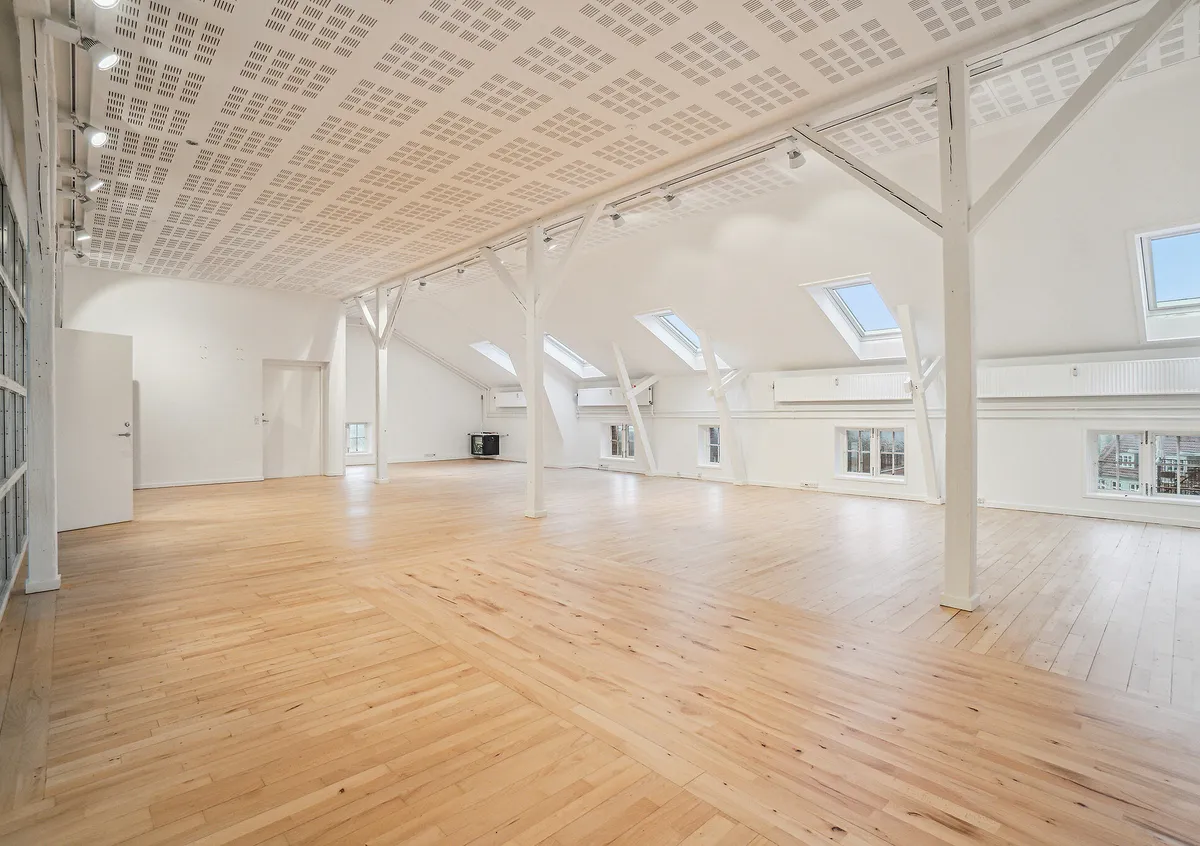 Lyst og højloftet kontorrum med lyse, trægulve, hvide vægge og lofter samt store vinduer med naturlys. Lejemål på Viborggade 70, 4., 2100 København Ø.