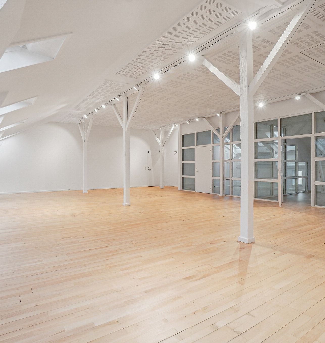 Lyst kontormiljø med højloft og trægulve. Hvid indretning med glasdøre og loftsvindue. Moderne lysekroner og gulve. Lyst og åbent rum til leje i København