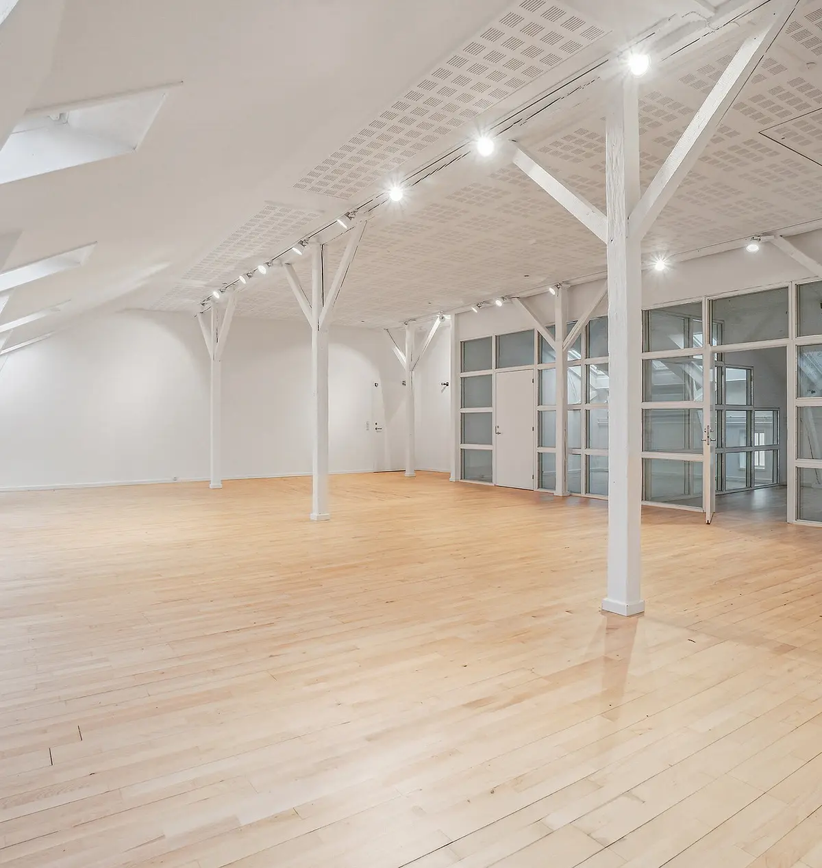 Lyst kontormiljø med højloft og trægulve. Hvid indretning med glasdøre og loftsvindue. Moderne lysekroner og gulve. Lyst og åbent rum til leje i København