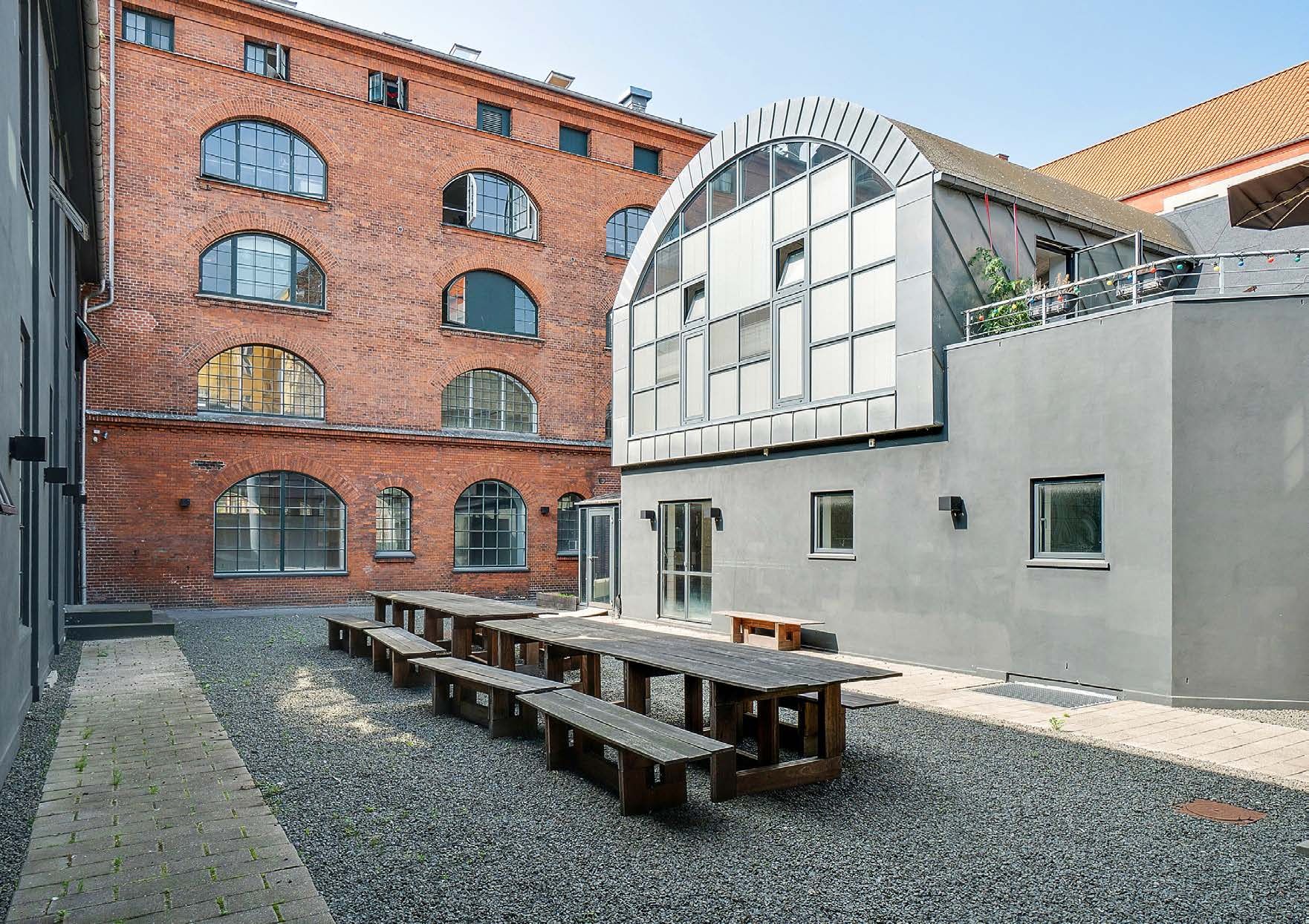 I lyst og højloftet kontormiljø på Viborggade 70, 4. i København Ø er der lange træbænke og træborde. Det er en tidligere fabriksbygning med røde mursten og lyse vinduer.