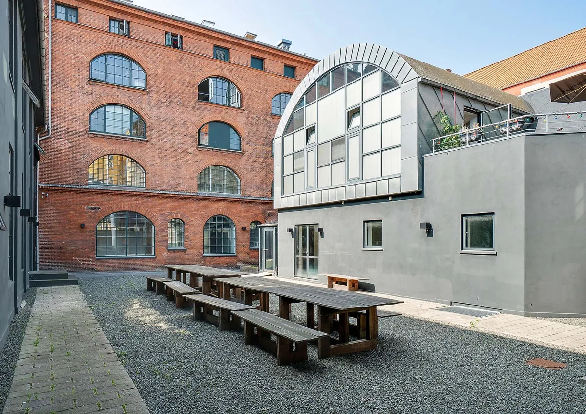 I lyst og højloftet kontormiljø på Viborggade 70, 4. i København Ø er der lange træbænke og træborde. Det er en tidligere fabriksbygning med røde mursten og lyse vinduer.