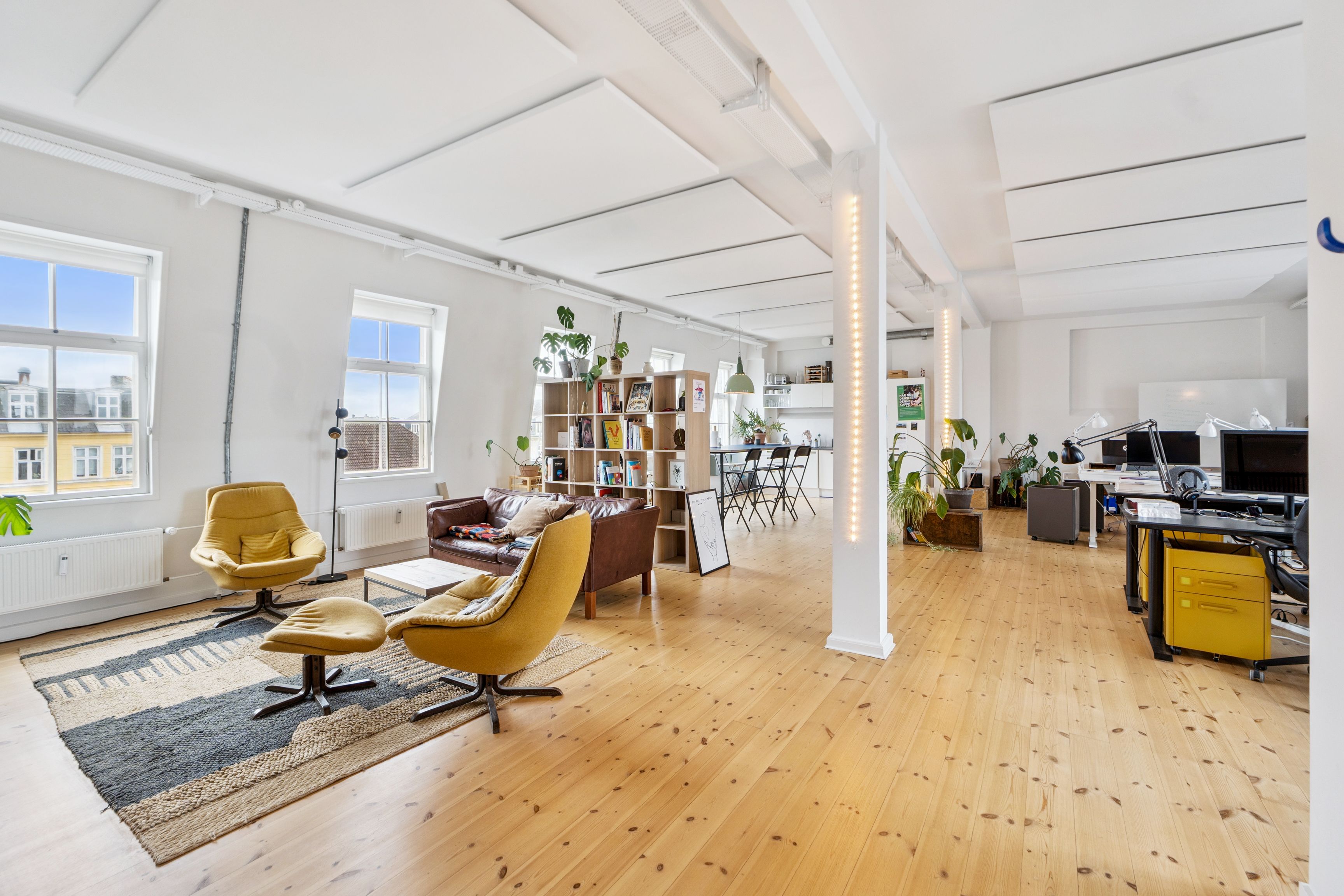 Kreativt kontor med højt til loftet, masser af vinduer og lysegule stole i moderne stil. På gulvet ligger tæppe og der er masser af plads til møder og arbejde