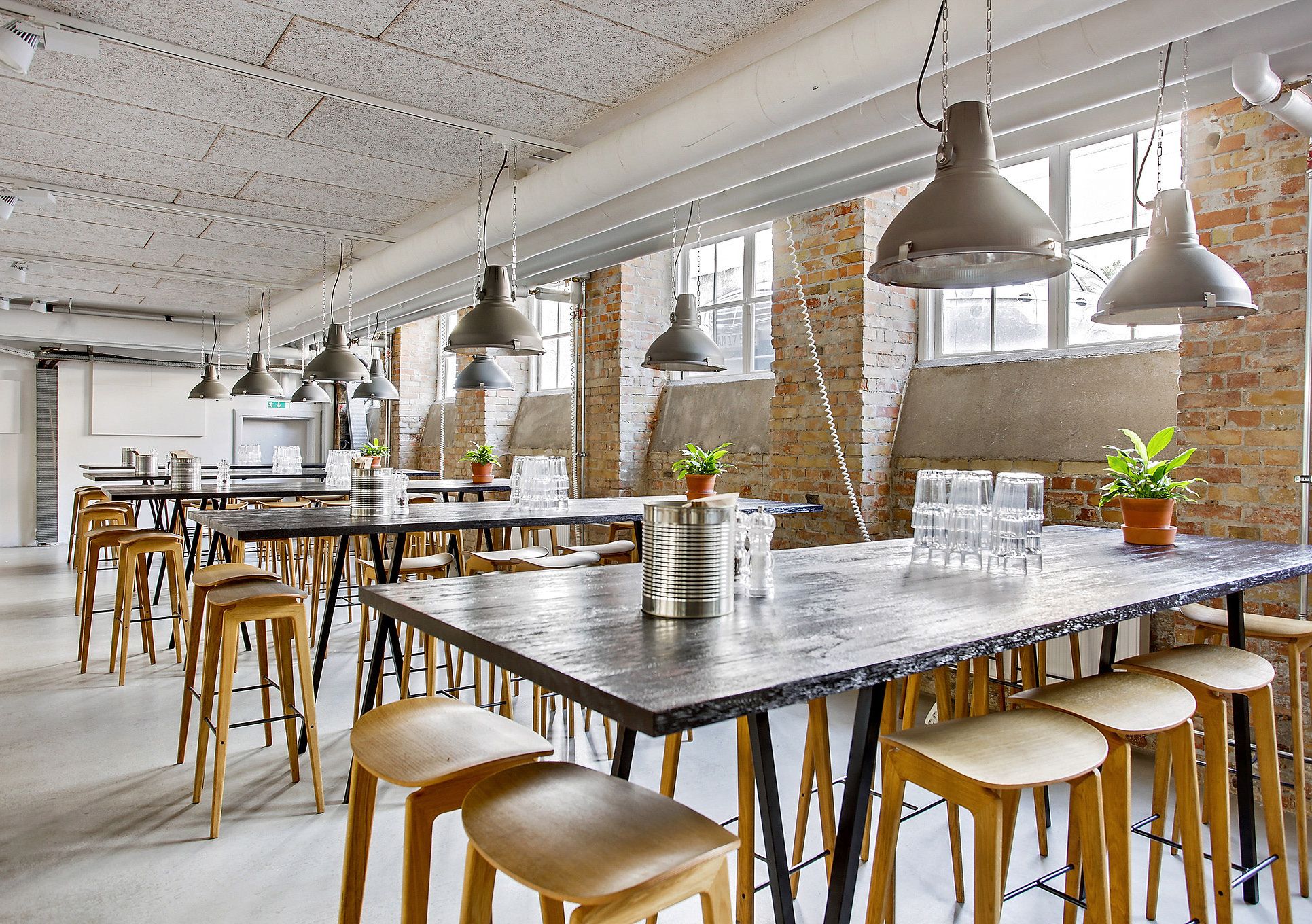 Stort kontor med industrielle loftslampe, lyserøde mursten og træstole. Store vinduer og naturligt lys. Vintage møbler og lyserøde mursten.