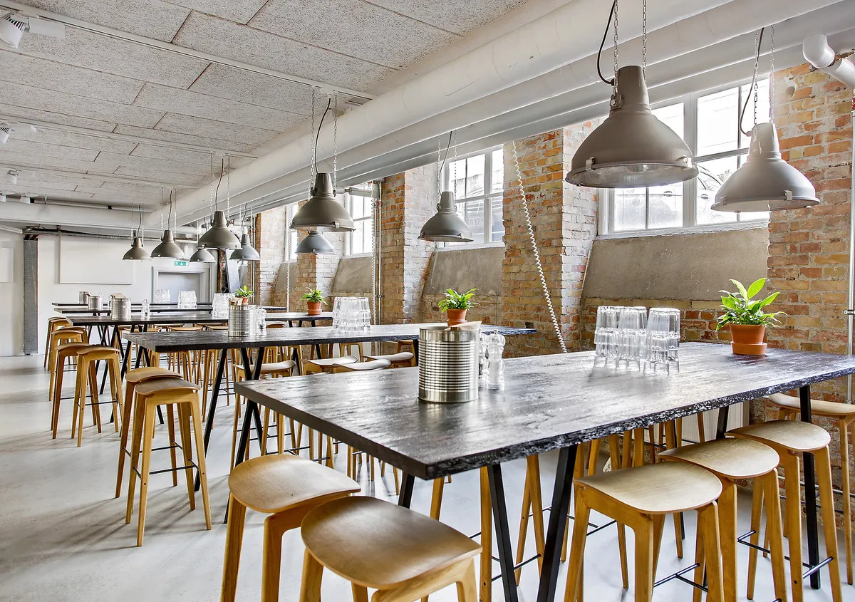 Stort kontor med industrielle loftslampe, lyserøde mursten og træstole. Store vinduer og naturligt lys. Vintage møbler og lyserøde mursten.