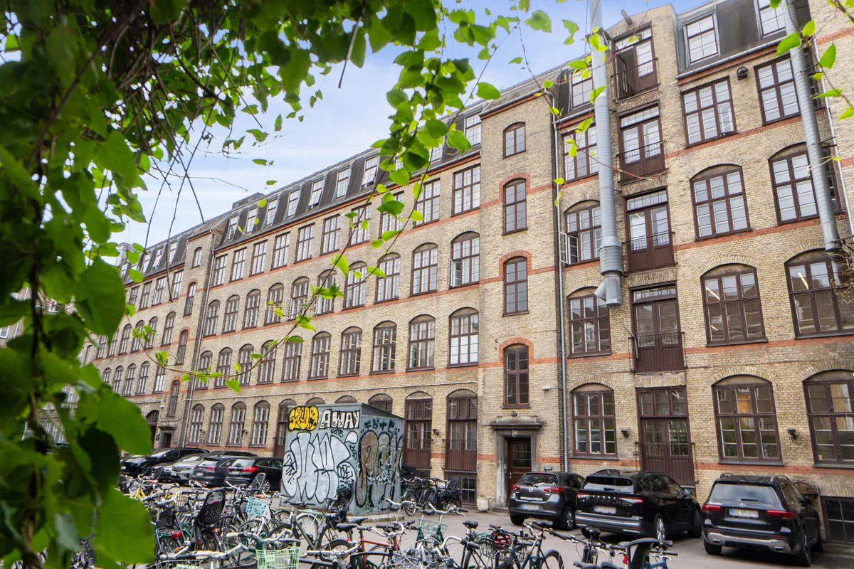 Mange cykler parkeret foran et stort bygningskompleks med store vinduer og graffiti på facaden