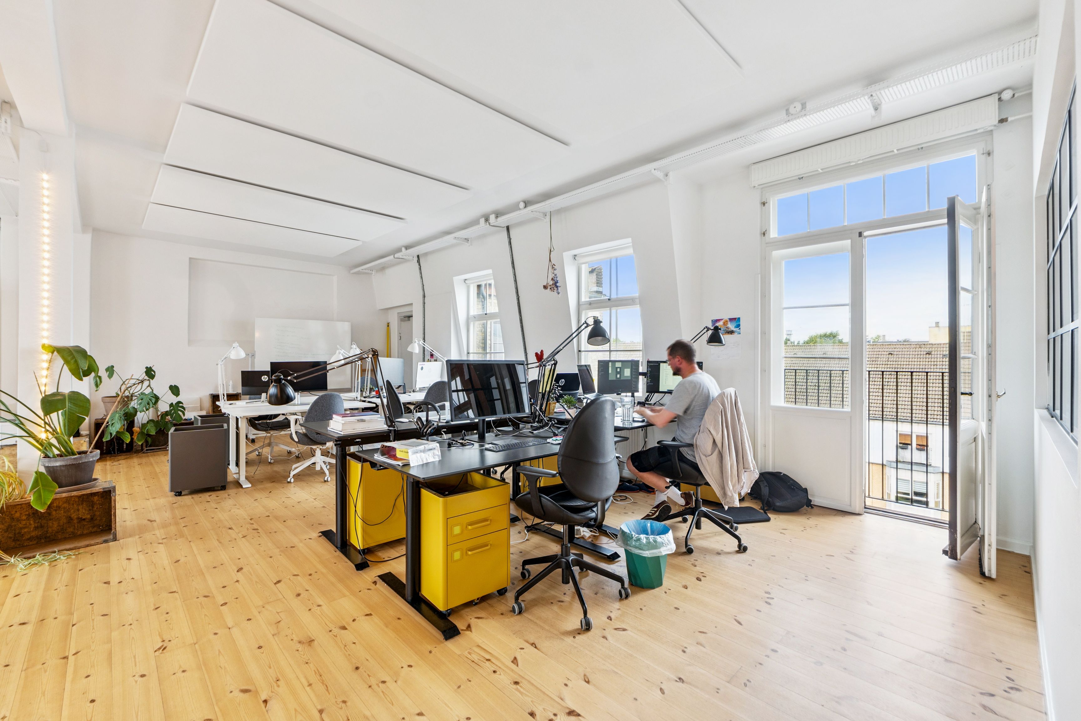 To mænd arbejder i et minimalistisk kontor med højt loft, moderne møbler, planter og lyse vinduer.