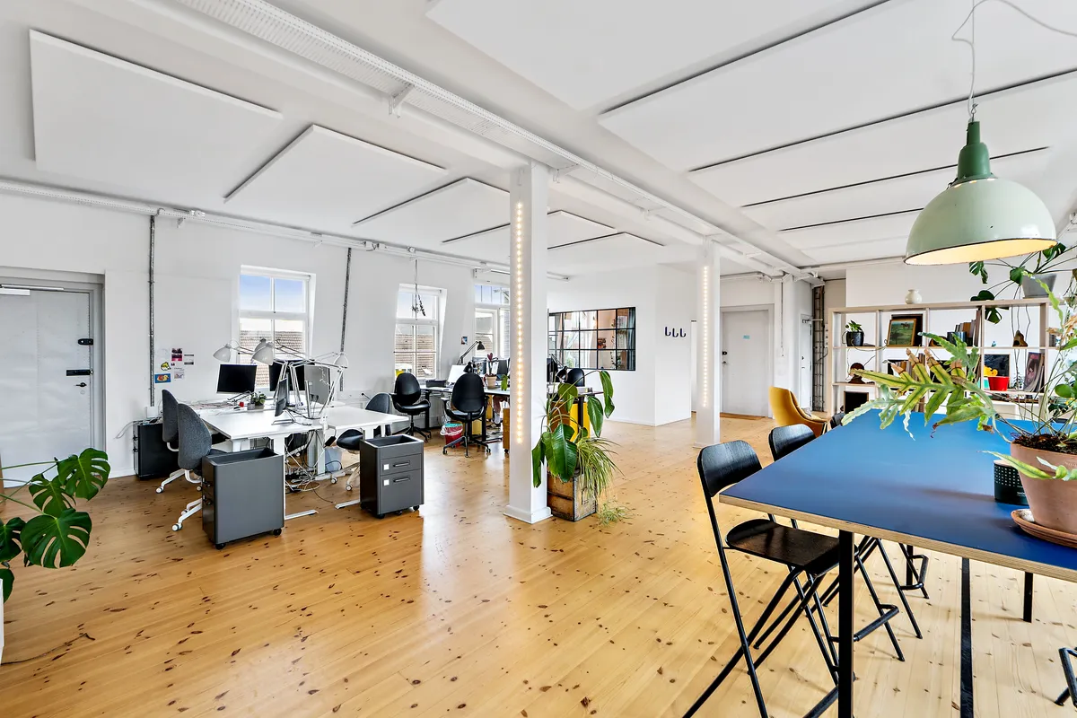 Flot kontor med lyse lofter og trægulve, store vinduer og møbler i moderne design, plantepot med grønne planter og en lysekron med grøn kuppel