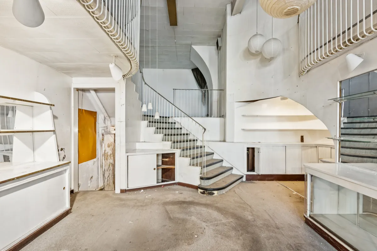 To-etagers lokale med trappe og åbne sektioner. Dekorative lysekroner hænger fra loftet. Forskellige rum og gavle er lyse og inviterende.