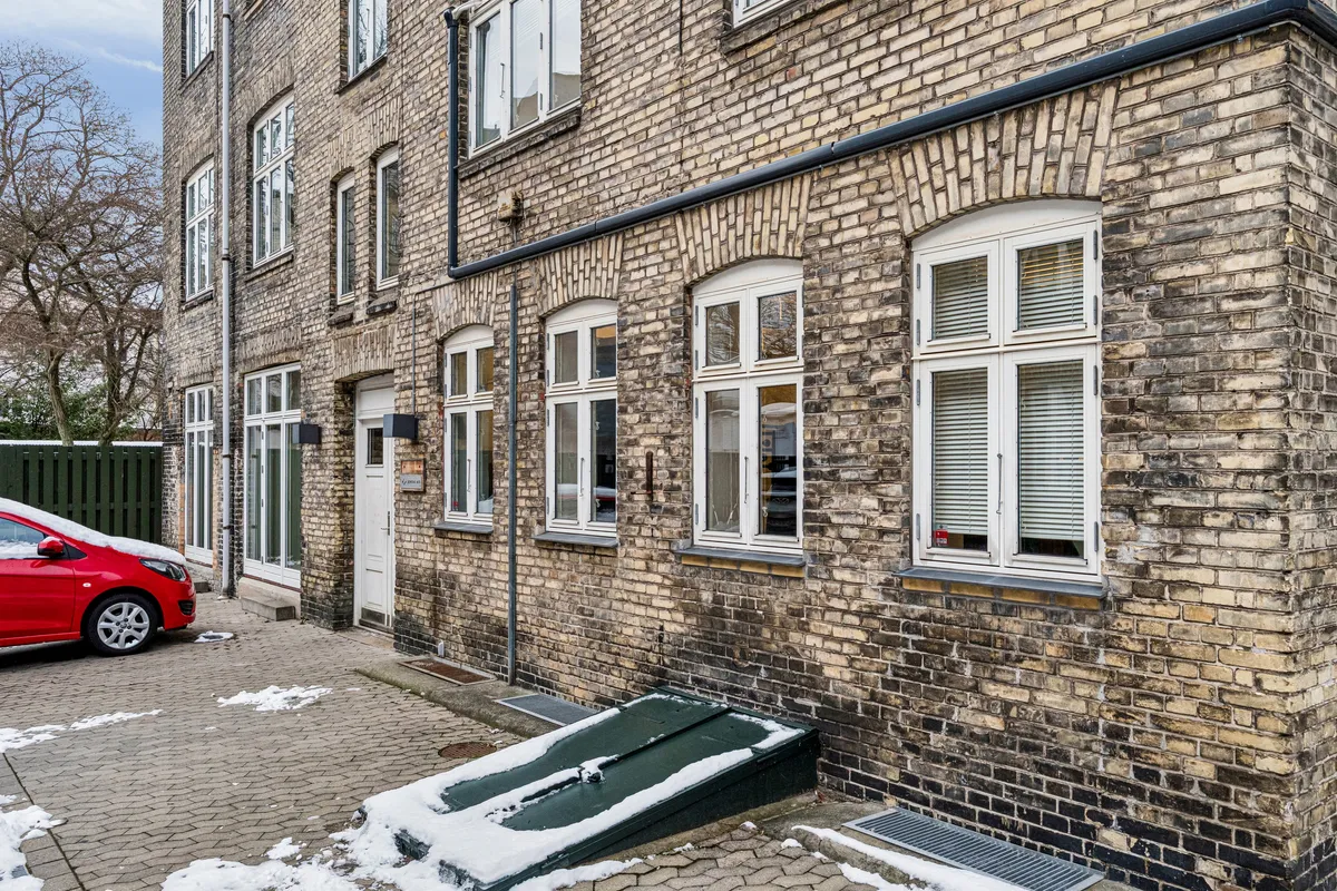 Kontorbyggeri med røde mursten og hvide ruder på Smallegade 46B. Det er en fredelig og lukket gård, og der er sne på gågaden.