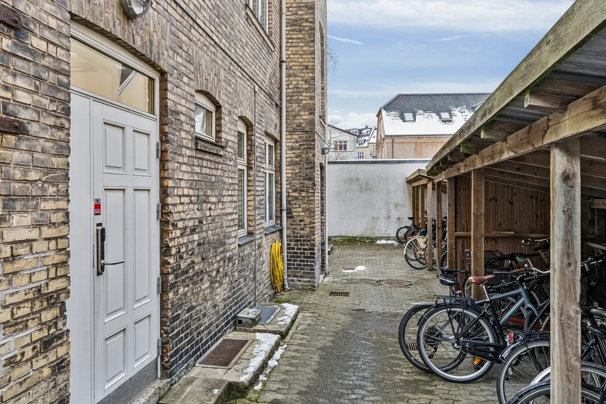 Garage med to cykler parkeret og et stort hvide dør i baggård med træhytte og stående cykler