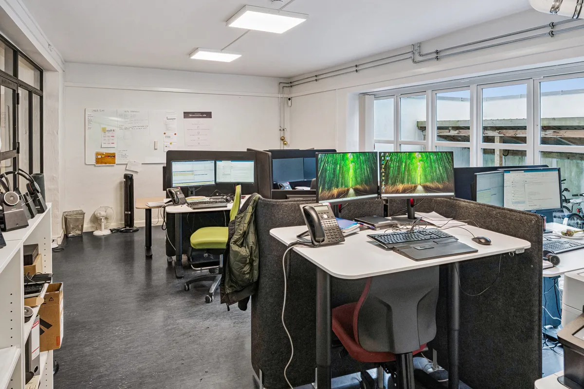 Kontor til leje med moderne møbler og teknologi i Frederiksberg. Billeder og papir på væggen og skrivebord. To skrivebord med computere og telefoner.