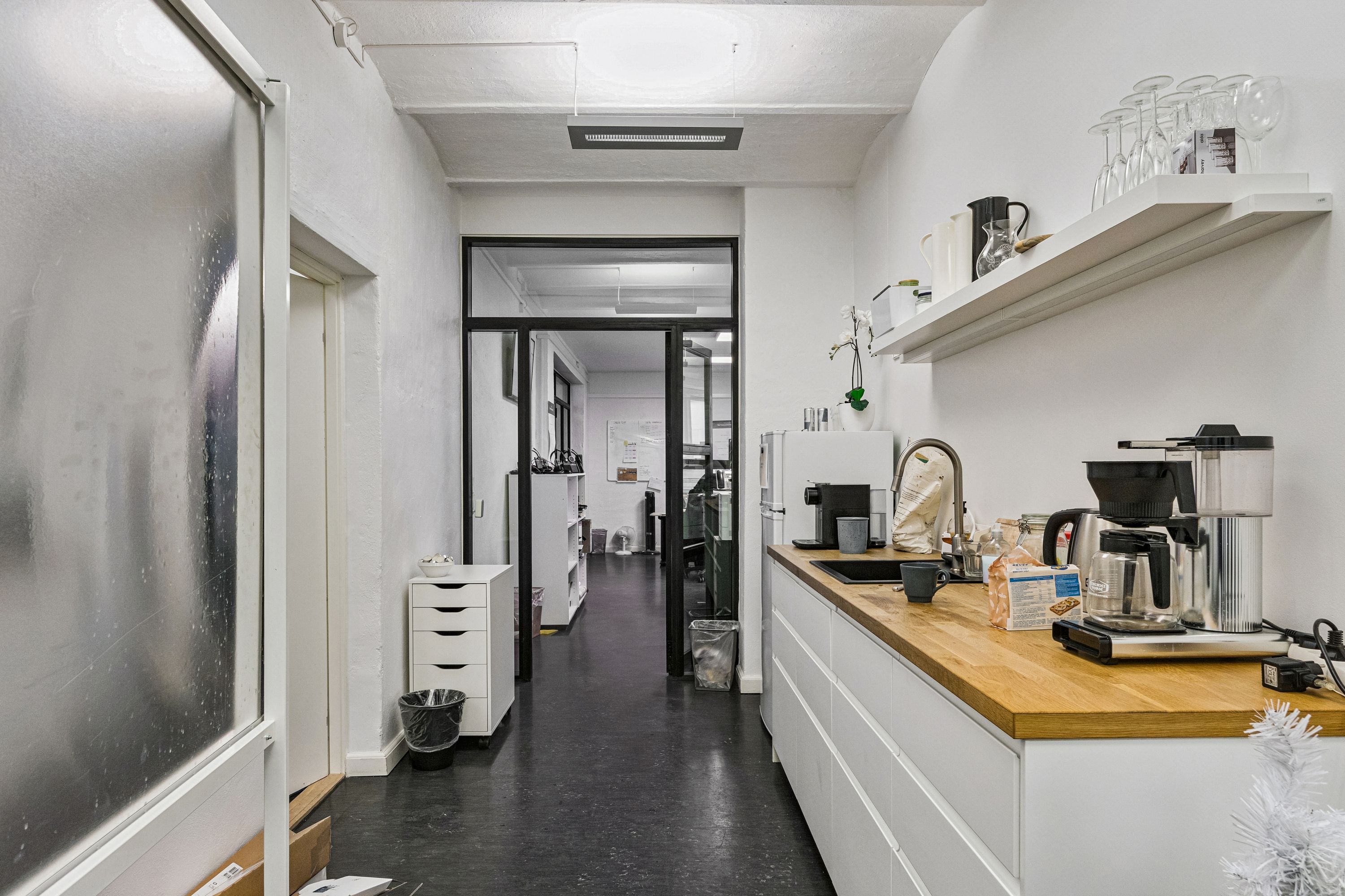 Kontor til leje i roligt baghus med hvidt køkken og lyse lofter, og med skrivebord og skraldespand i baggrunden