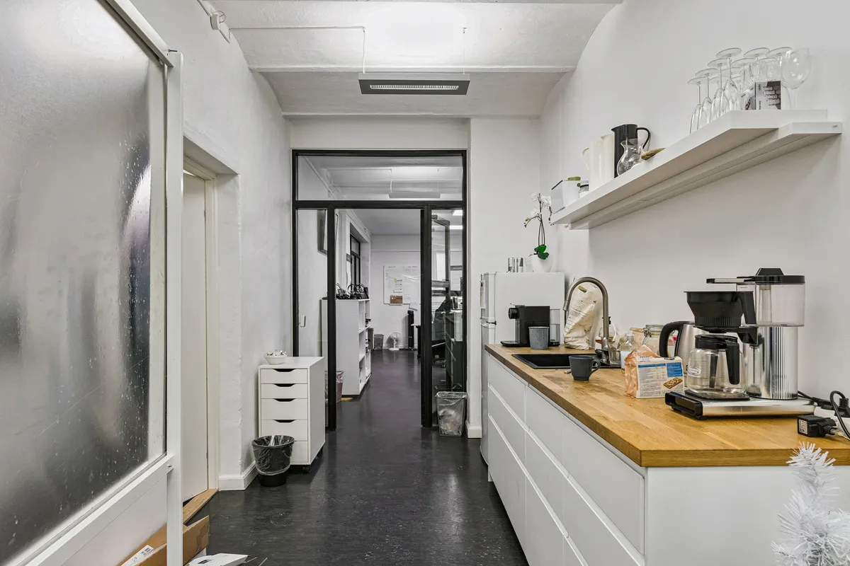 Kontor til leje i roligt baghus med hvidt køkken og lyse lofter, og med skrivebord og skraldespand i baggrunden