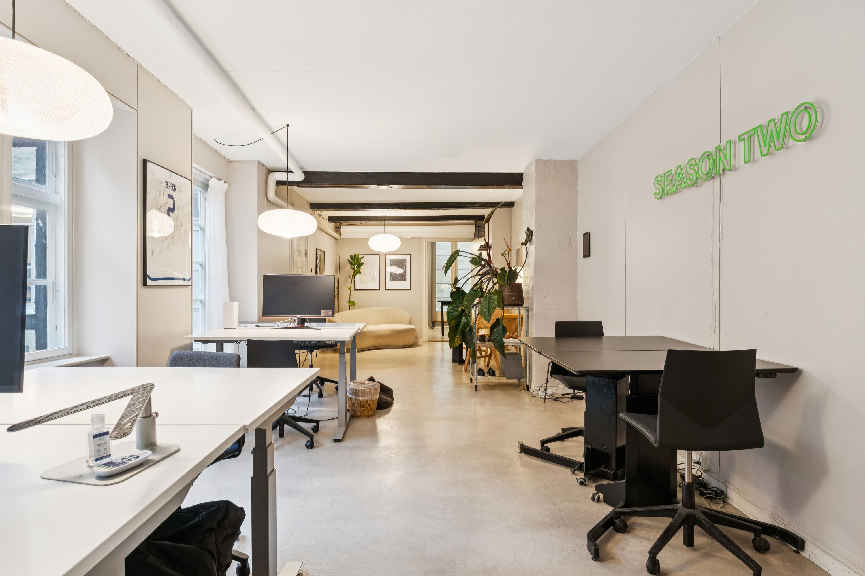 Kontor med lyse loftslampe og møbler i lyse farver. En stol står foran en bord med en computer. Planter og en tekst på væggen.