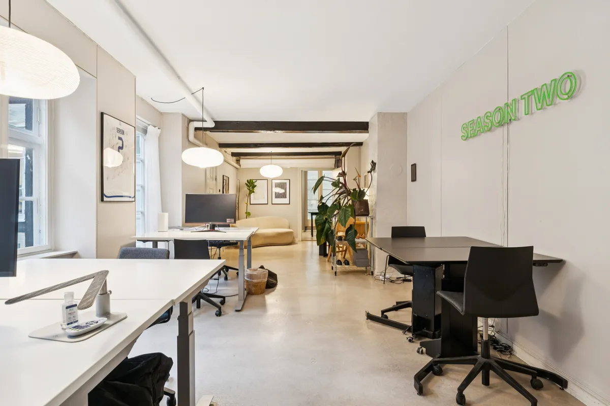 Kontor med lyse loftslampe og møbler i lyse farver. En stol står foran en bord med en computer. Planter og en tekst på væggen.