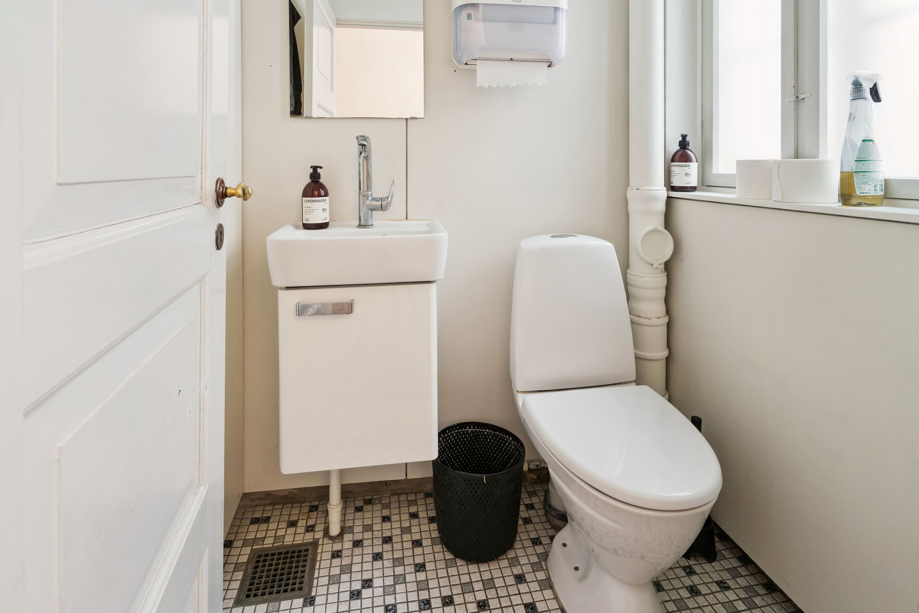 Ren toiletrum med hvid toilet, hvidt vask og to toiletpapirruller på vindueskarme