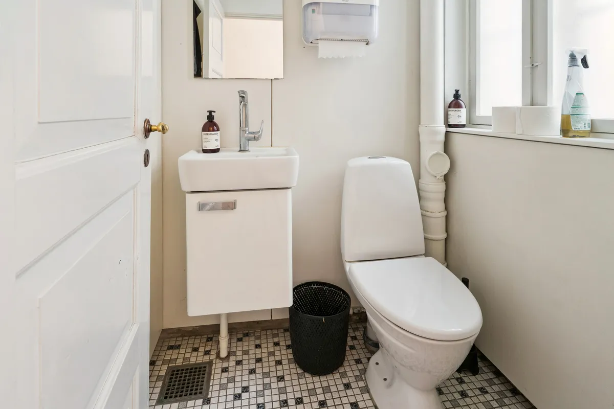 Ren toiletrum med hvid toilet, hvidt vask og to toiletpapirruller på vindueskarme