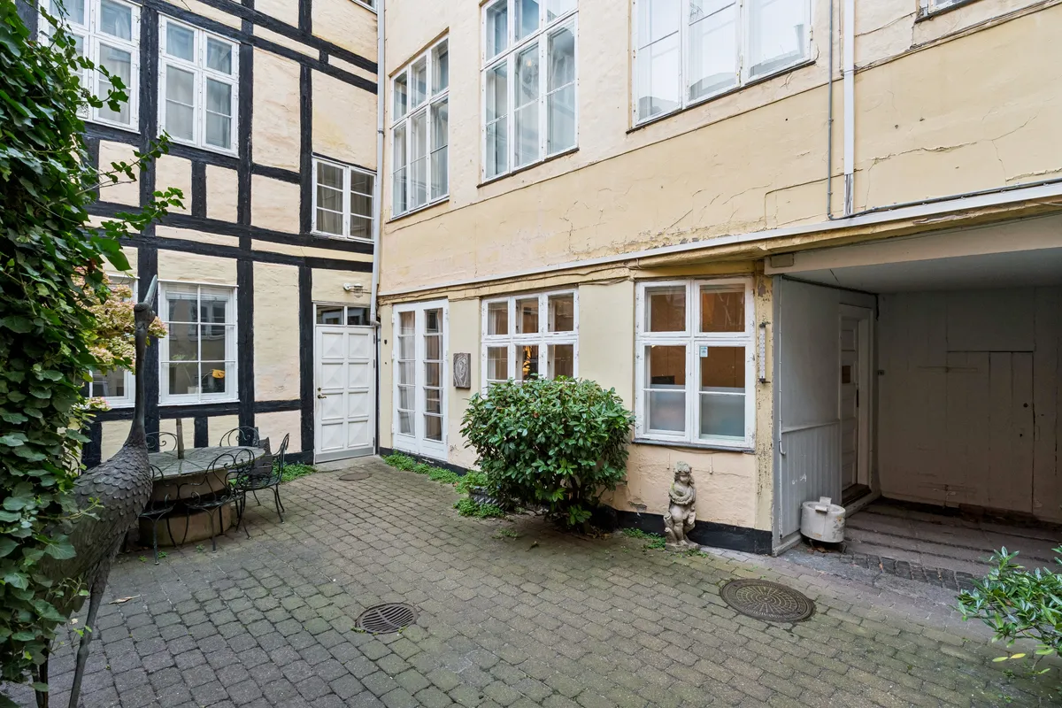 Kontorlejemål med indgang til baghaven, stort træbord og stole, stenbrolægning og statue på gården, to bygninger med hvide og sorte vægge og vinduer