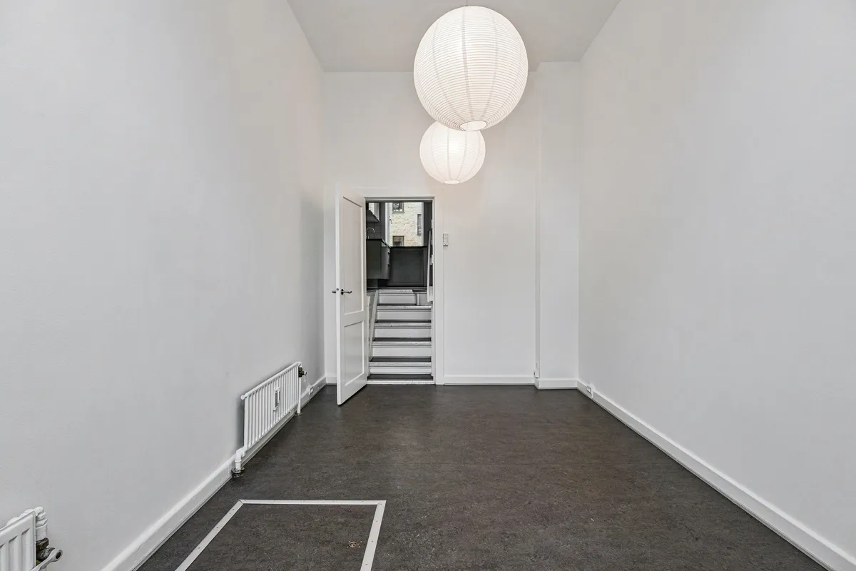 En stor stue med højloft og åben dør til gården. To hvide kuglepærer hængende på loftet og en hvid radiator på højre side