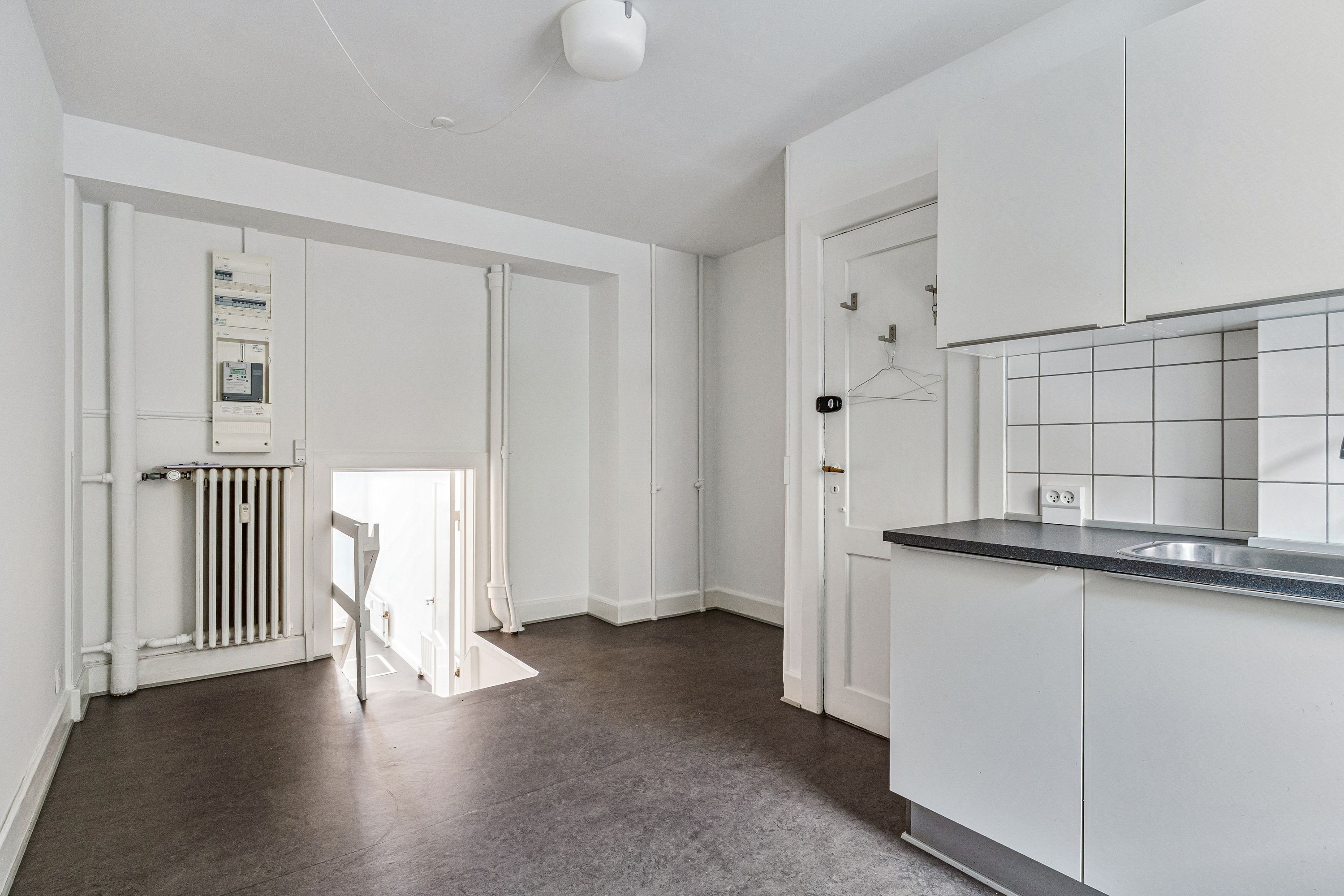 Lejlighed med højloft og minimalistisk design i Frederiksberg. Værelse med hvidt loft og vægge, høj hvid garderobe og spisestue med moderne udsmykning og lys.
