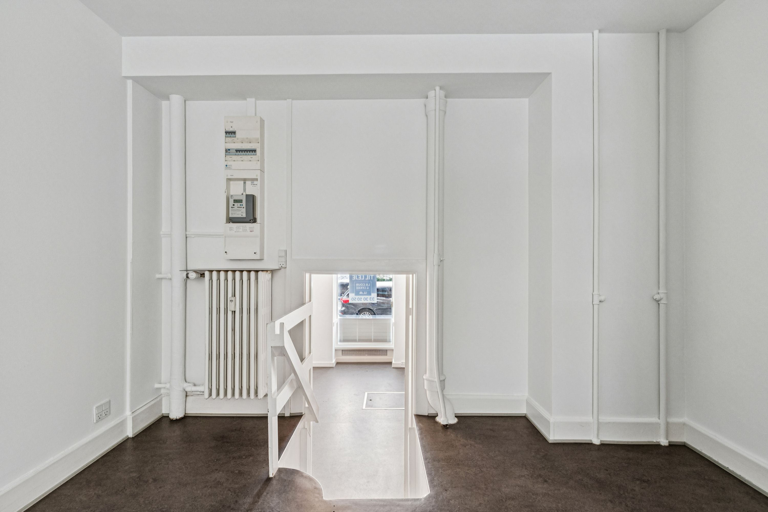 En lyse hvid indgangsdør med trappetrin i en højloftet og nyrenoveret butikslokal med et fint baglokale mod gården