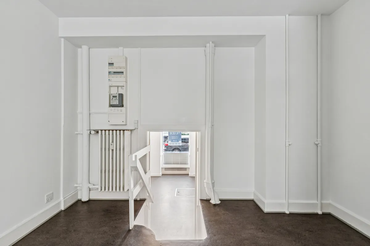 En lyse hvid indgangsdør med trappetrin i en højloftet og nyrenoveret butikslokal med et fint baglokale mod gården