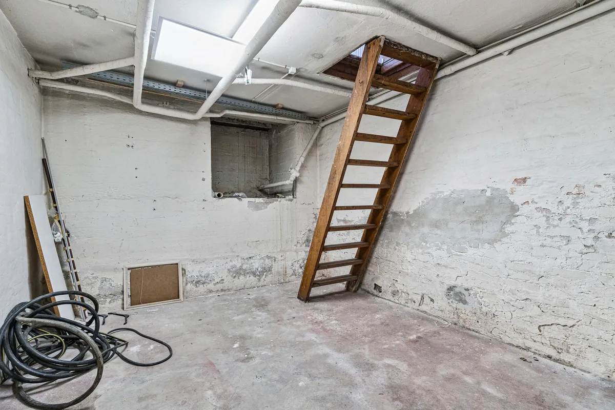 Lagerrum med loftsrum og stige. Væggene er revnet og snavsede. Der er røgskader og et gammelt træklatretårn.