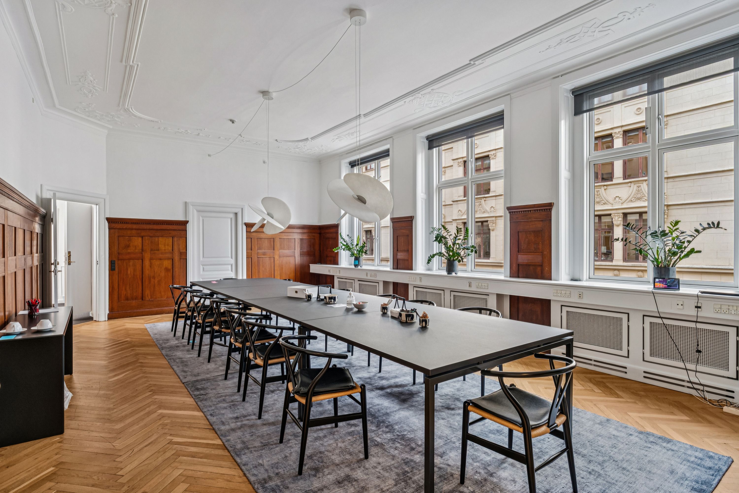 Herskabeligt kontor med elegant møblering, moderne skrivebord, møbler i lyse farver og moderne loftslampe samt en udsigt til byen.