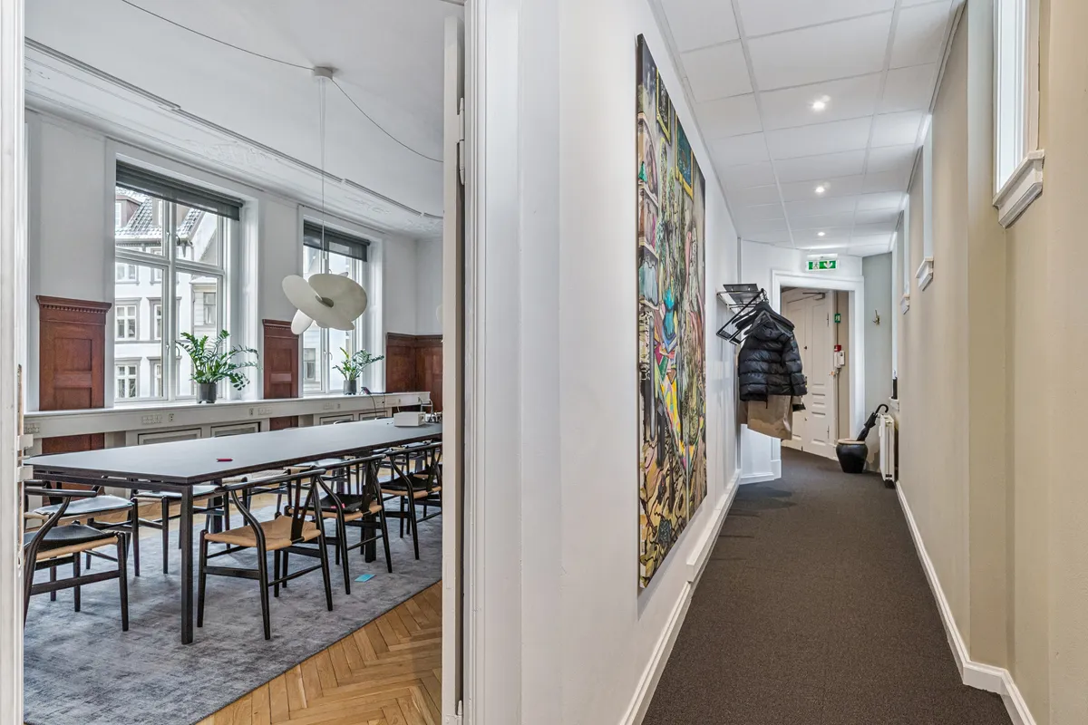 Langt kontor med massivt bord og stole og lyseruder med plantager og udsigt til gaden og lysekroner