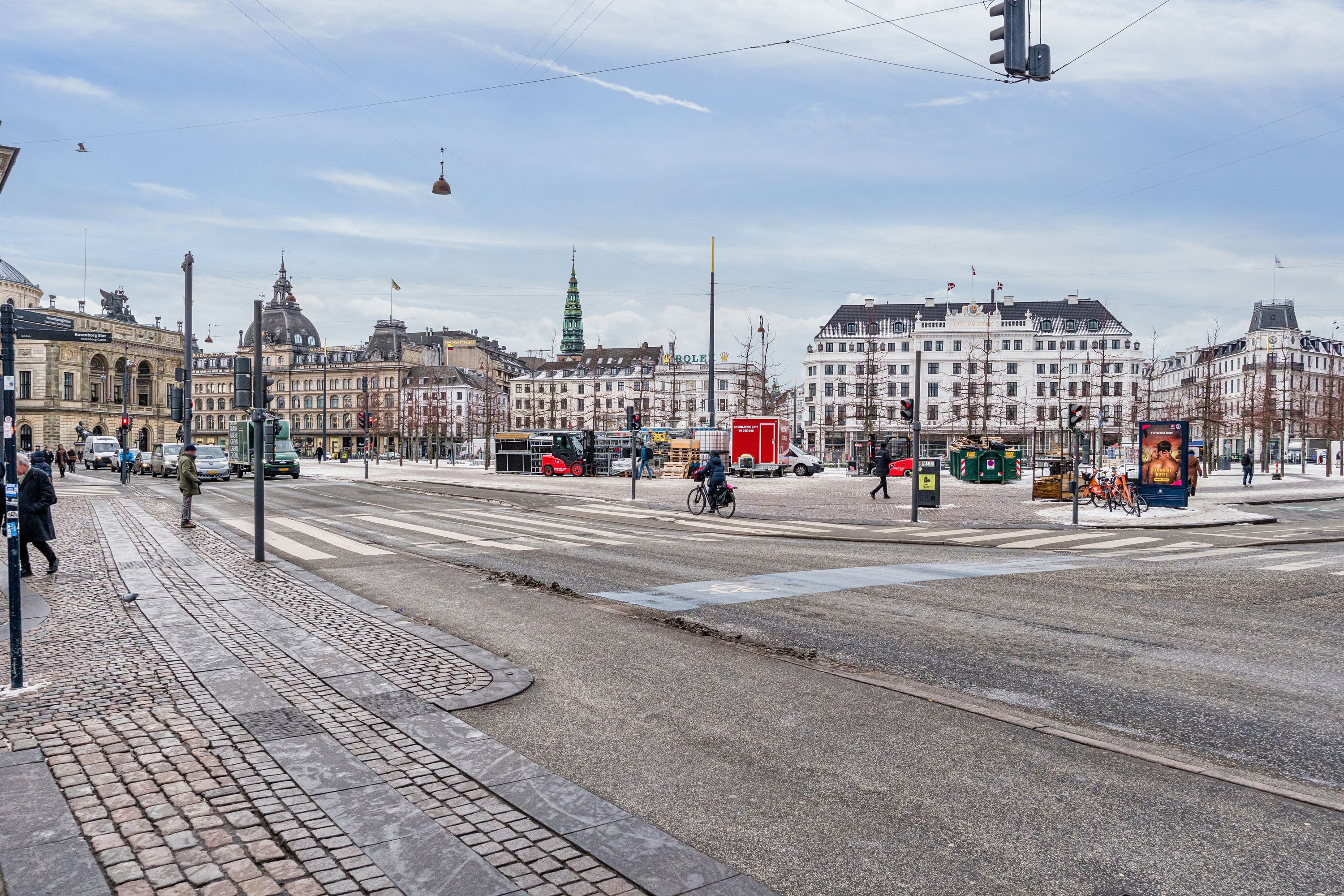 Bredgade med kontorer og gågade, folk og cykel, røde og hvide biler, rødt sporvogn og skilte