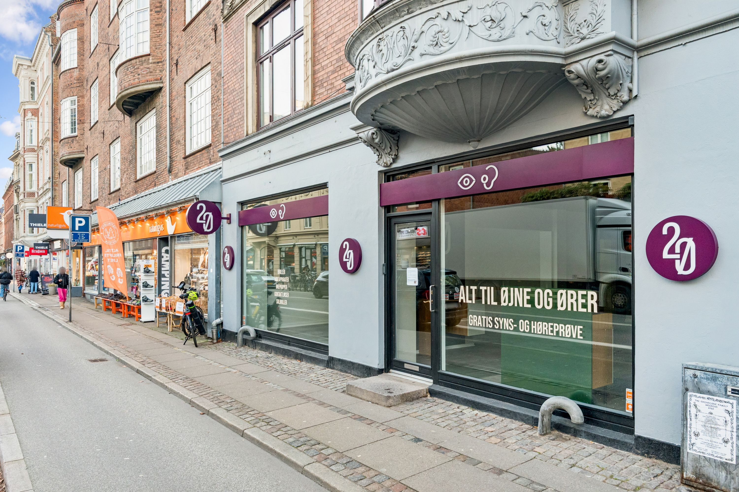 Gammel Kongevej med 4D-butik, forretningslokaler og gågade, hvor folk går og cykler langs gaden med parkerede biler og reklamebanner