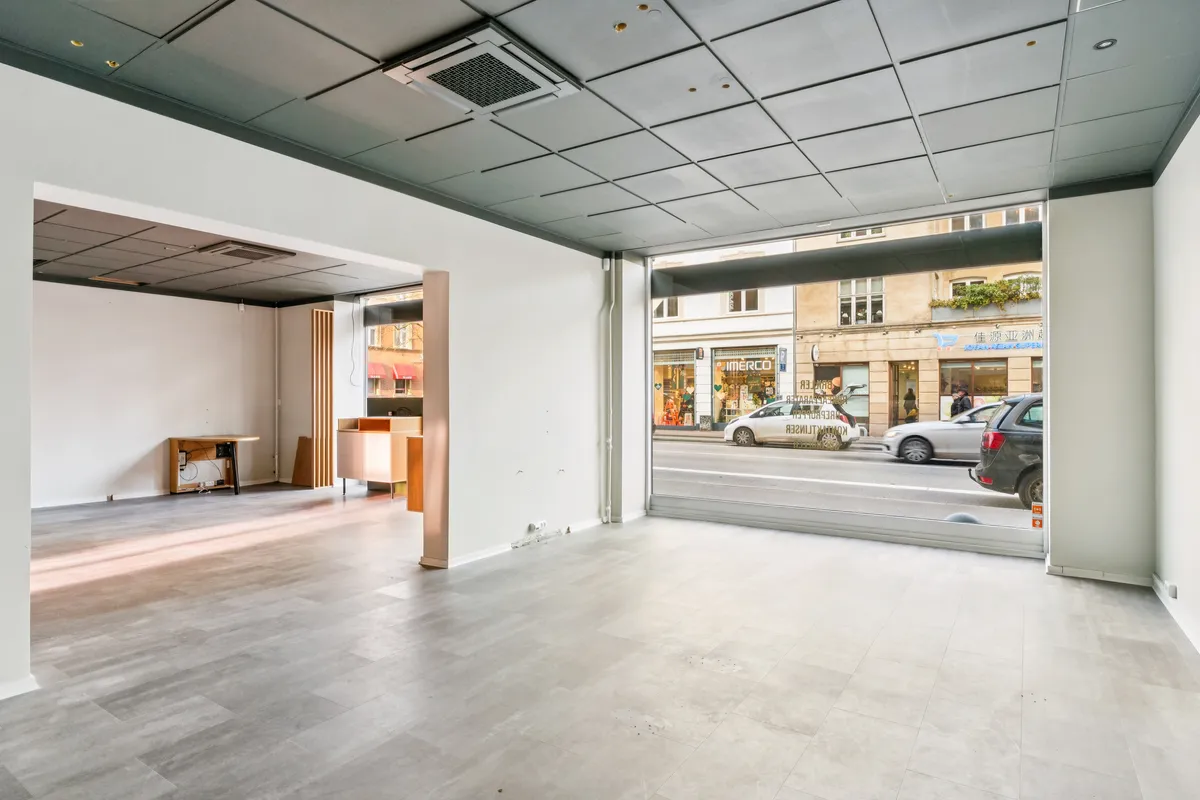 En moderne, kølig butik med glasdør og åben indgang til en bred gade med biler og bygninger