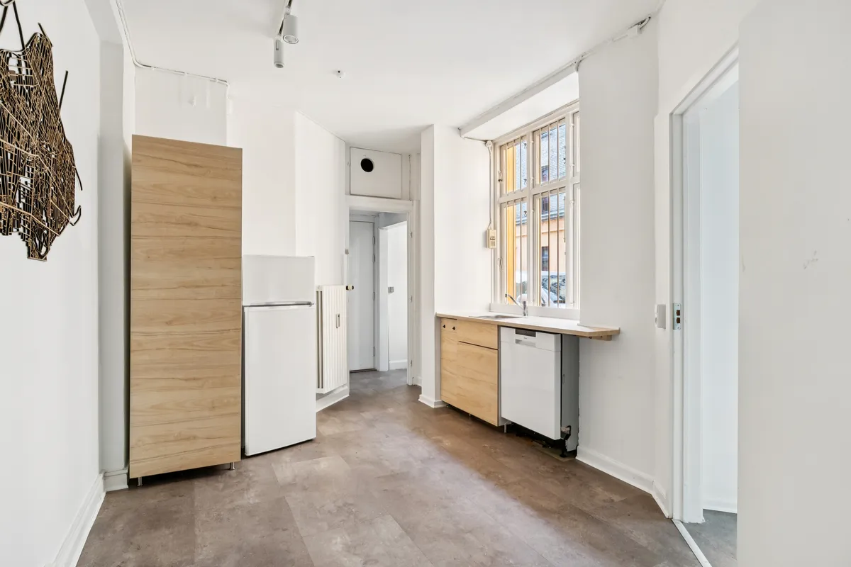 En moderne, lys og rummelig køkken med hvide vægge, lyse gulvfliser, en hvid køleskab og en trækøkken.